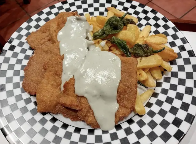 Escalope con salsa cremosa, patatas fritas y pimientos fritos en plato de cuadros