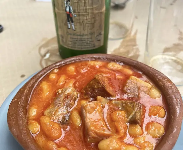 Fabada con una botella de sidra al fondo
