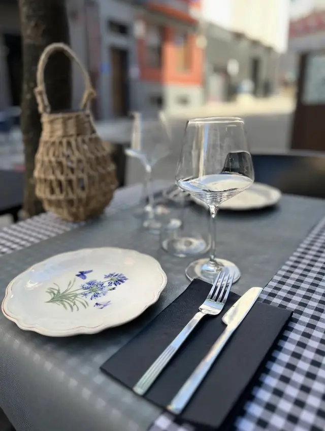 Mesa de terraza con mantel de cuadros, plato con flores azules, copa y servilleta negra