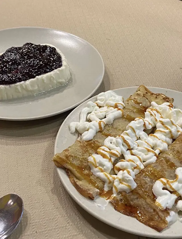 Dos postres sobre la mesa: uno con frutos rojos sobre base blanca y otro de crepes con nata y caramelo