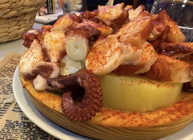 Pulpo con pimentón sobre cama de patata, servido en tabla de madera