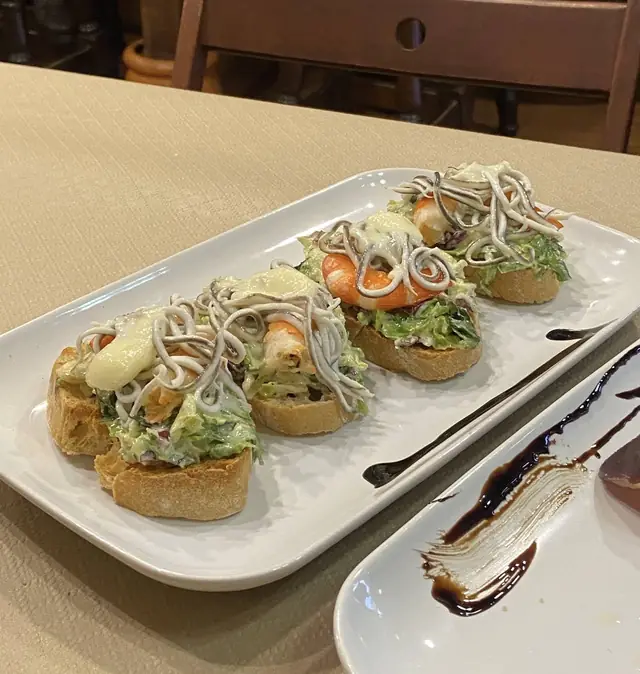 Cuatro tostas con lechuga, langostino y gulas sobre una bandeja alargada